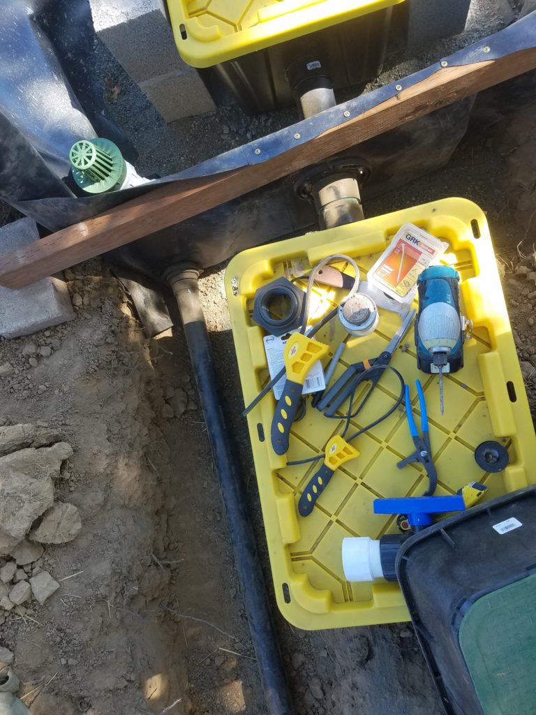 The green-screened inlet to the overflow is in the upper right, and the black pipe leading to the outlet is seen adjacent to (above in photo) the pump bin. A pressure-treated 2x4 holds the liner up between the filter bin and the pump bin.